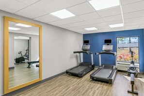 Un gimnasio con cintas de correr, un espejo y equipo de ejercicio.