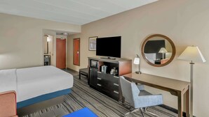 Una habitación de hotel con cama, escritorio, silla, televisor, espejo y lámpara.