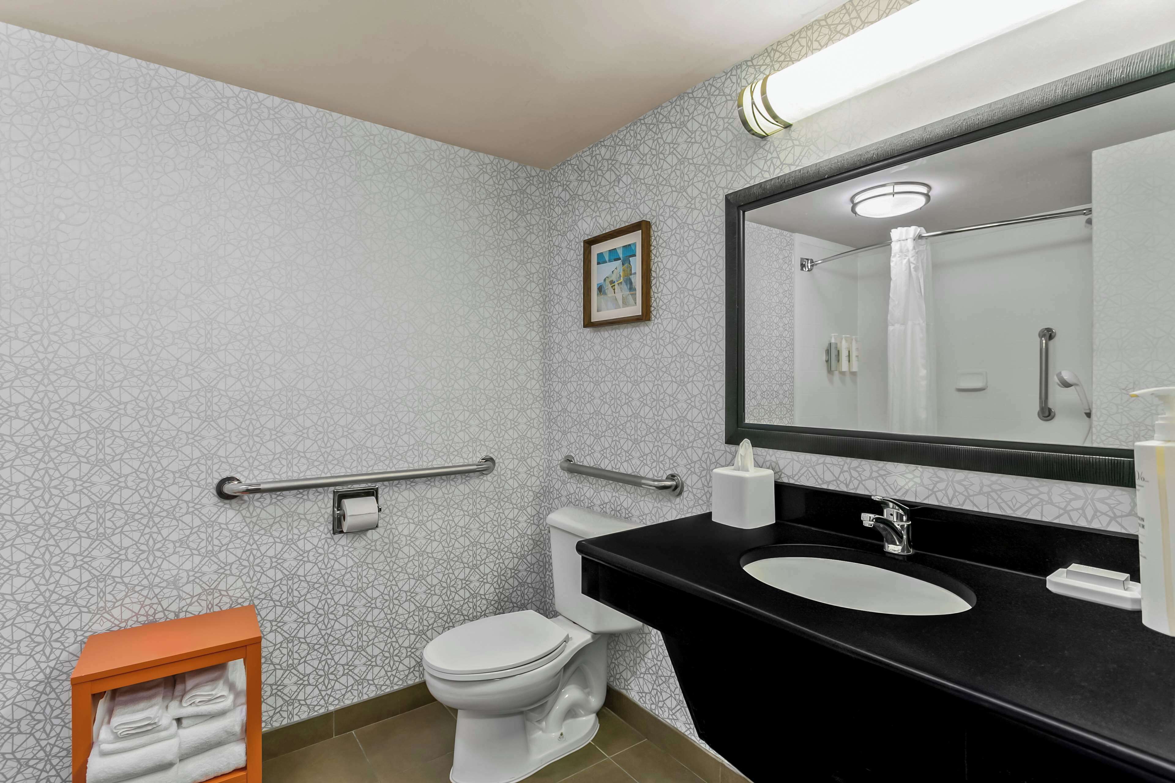 Et moderne badeværelse med tapetseret væg, et hvidt toilet, en sort vask og et spejl.