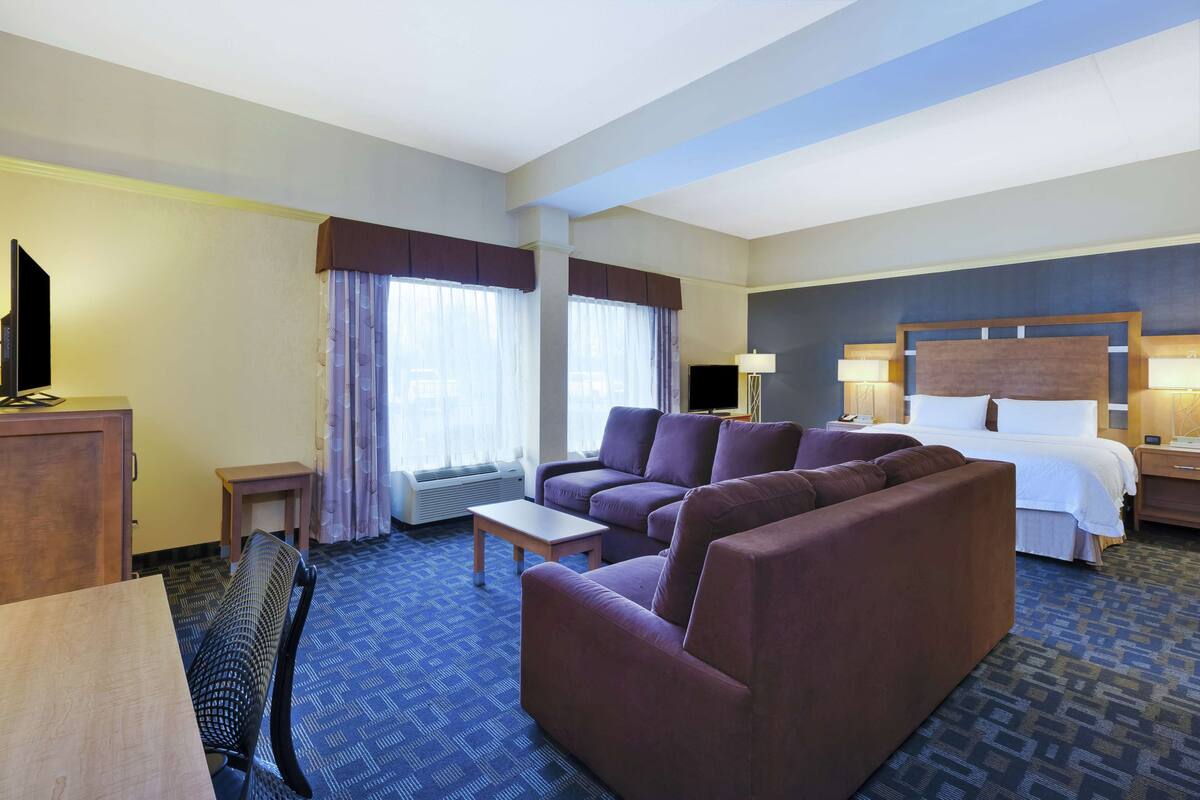 A hotel room with a large bed, a sofa, a desk, and a television.
