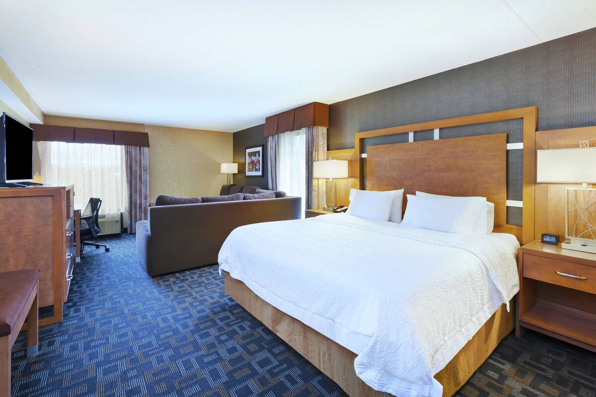 A hotel room with a large bed, a desk, a chair, a TV, and a lamp.
