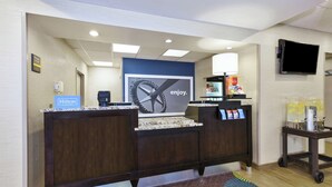 Zona de recepción de un hotel con un mostrador de madera oscura, un letrero azul que indica Hilton Honors, un reloj grande y una máquina de café.