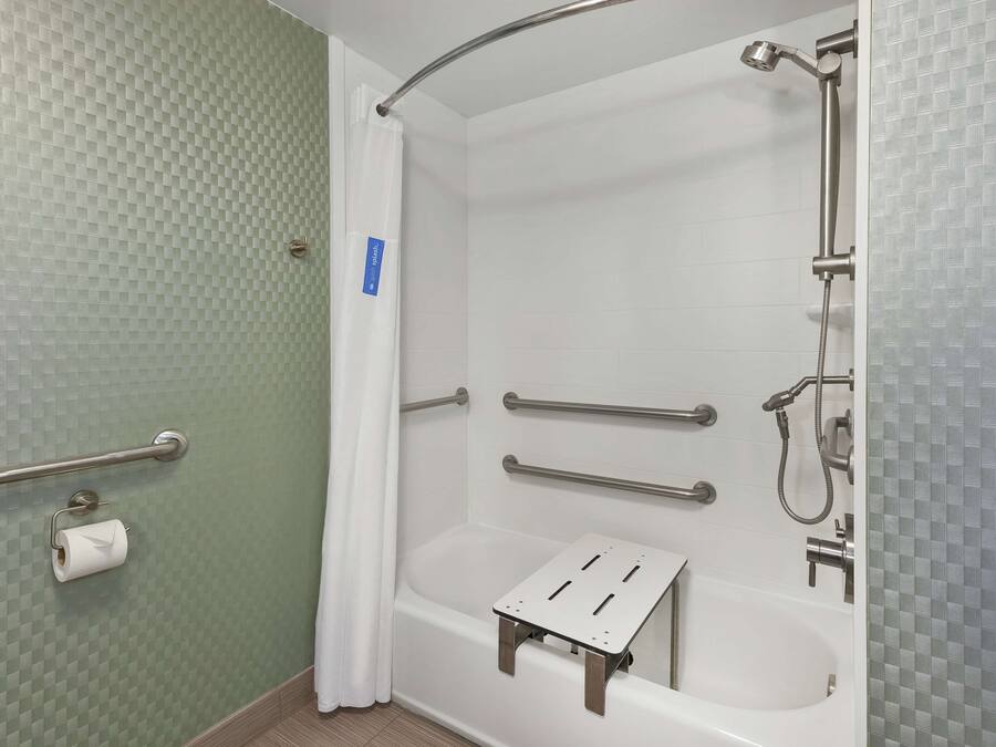 Un baño con ducha, barras de apoyo, porta papel higiénico y un escalón para accesibilidad.