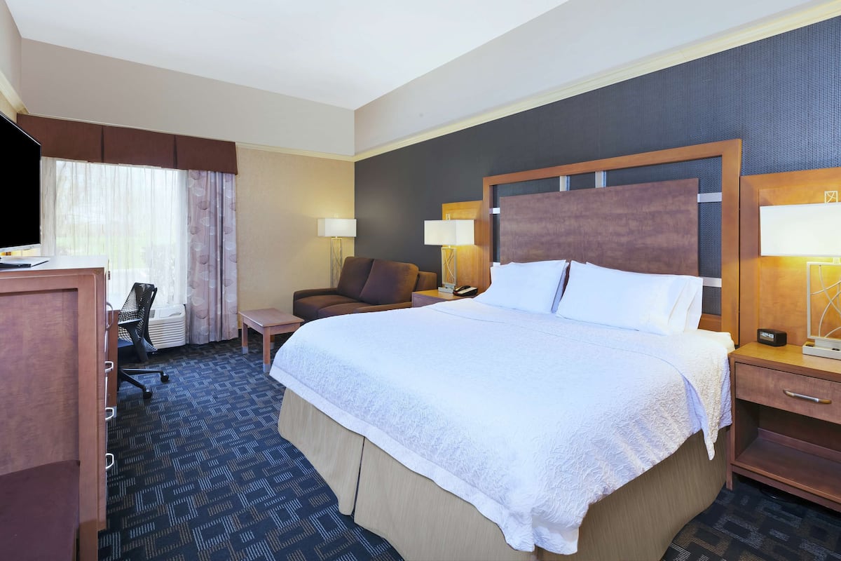 A hotel room with a large bed, a desk with a chair, a sofa, and two bedside tables with lamps.