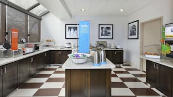 A modern kitchen with checkered flooring, a central island with a bowl of snacks, and a 'TASTE FOR MIXER LAUGH' sign.
