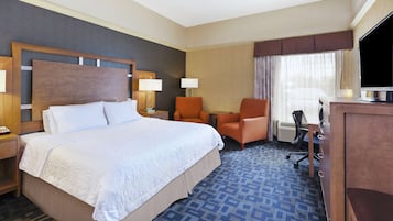 Een hotelkamer met een groot bed, twee stoelen, een bureau, een televisie en een raam met gordijnen.