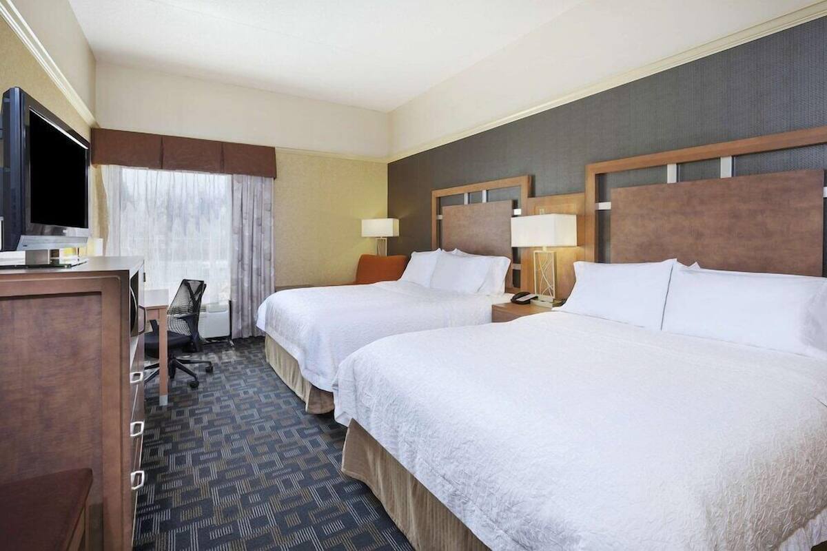 A hotel room with two beds, a desk, a TV, and a chair.