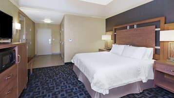 Une chambre d’hôtel avec un grand lit, un téléviseur posé sur une commode en bois, un bureau avec une lampe et une moquette à motifs.