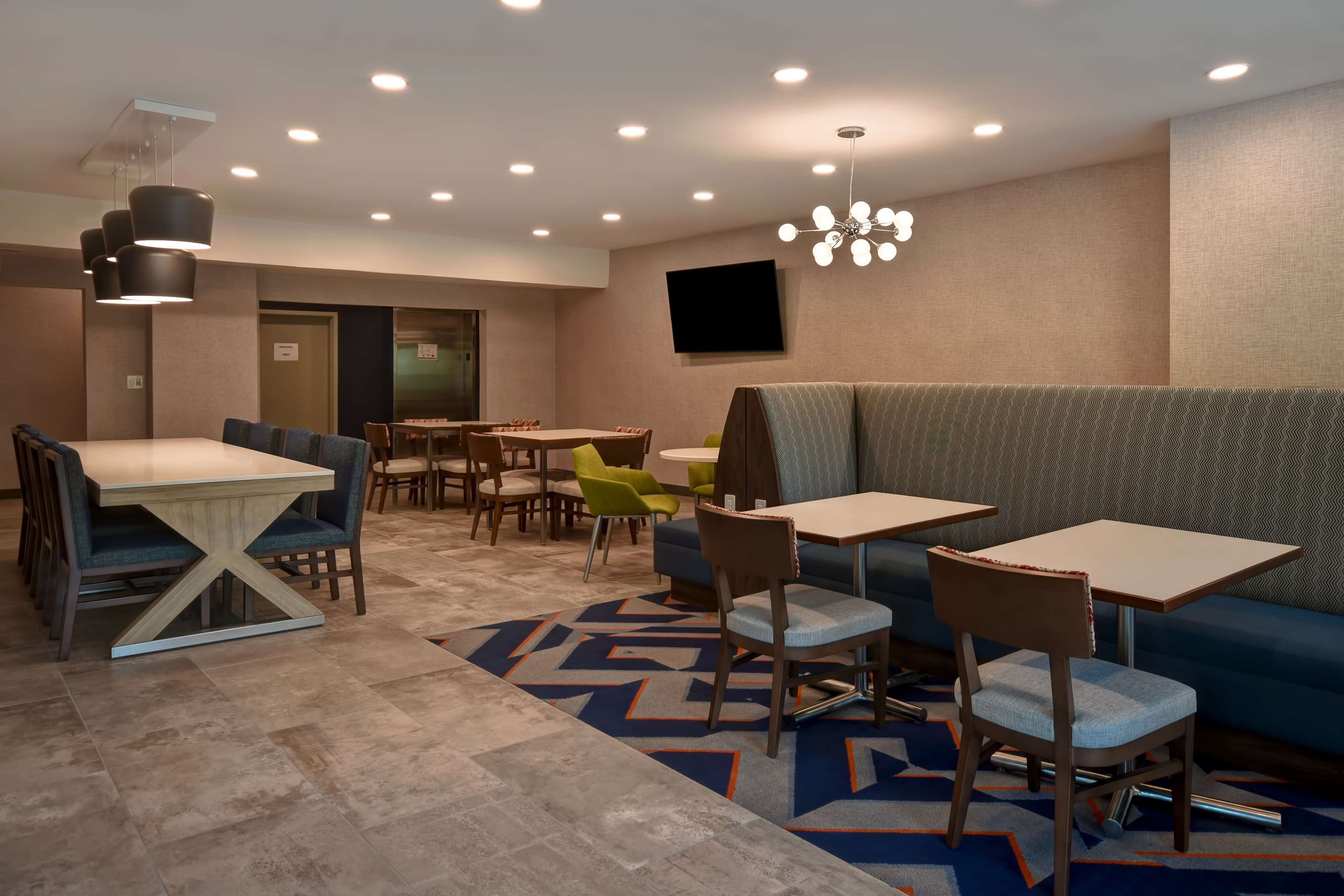 A modern dining area with multiple tables and chairs, a sofa, and a television mounted on the wall.