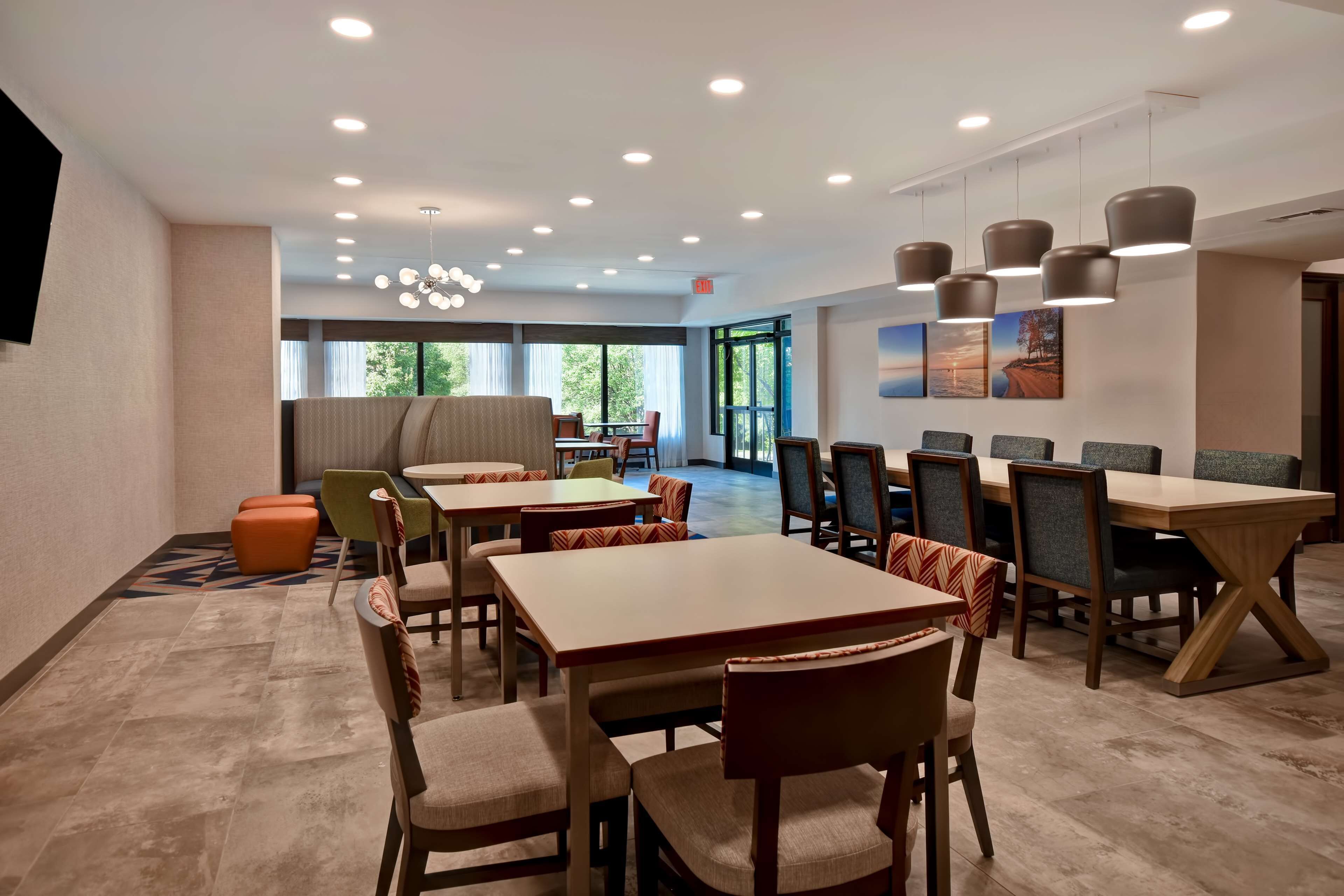 A modern dining area with multiple tables and chairs, recessed ceiling lights, and large windows providing natural light.