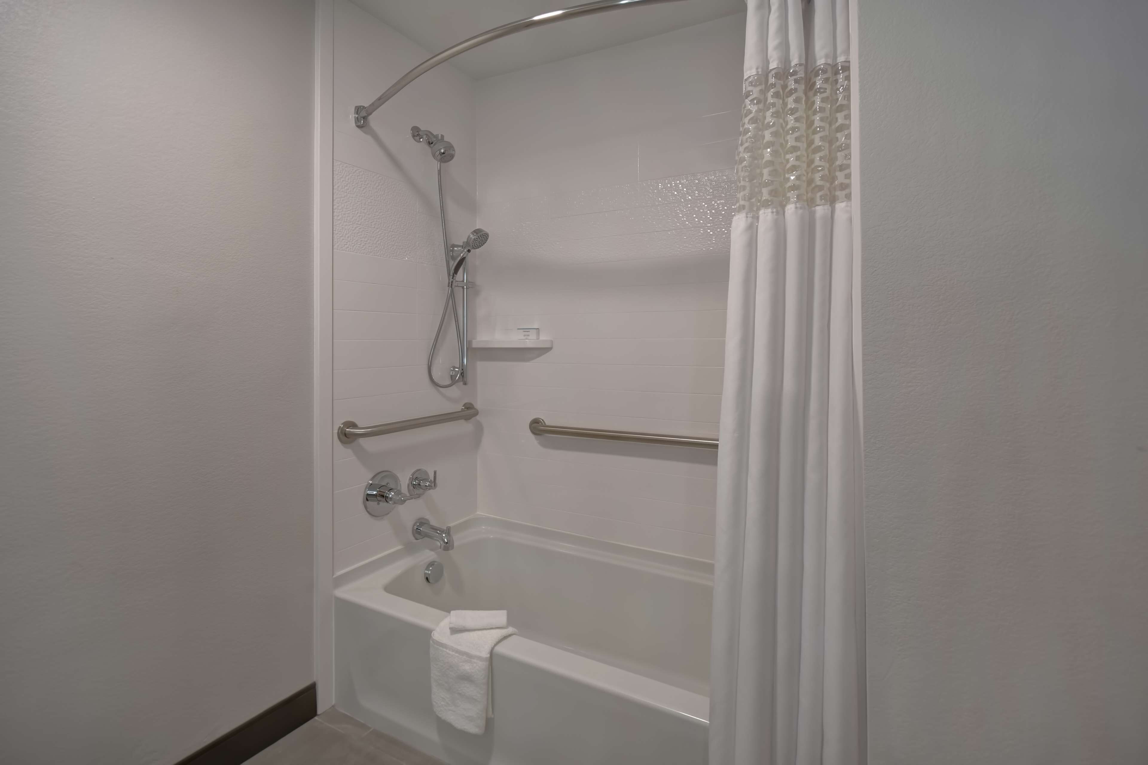 Un baño moderno con ducha a nivel del suelo, bañera y inodoro. Incluye barras de apoyo y un perchero para toallas.