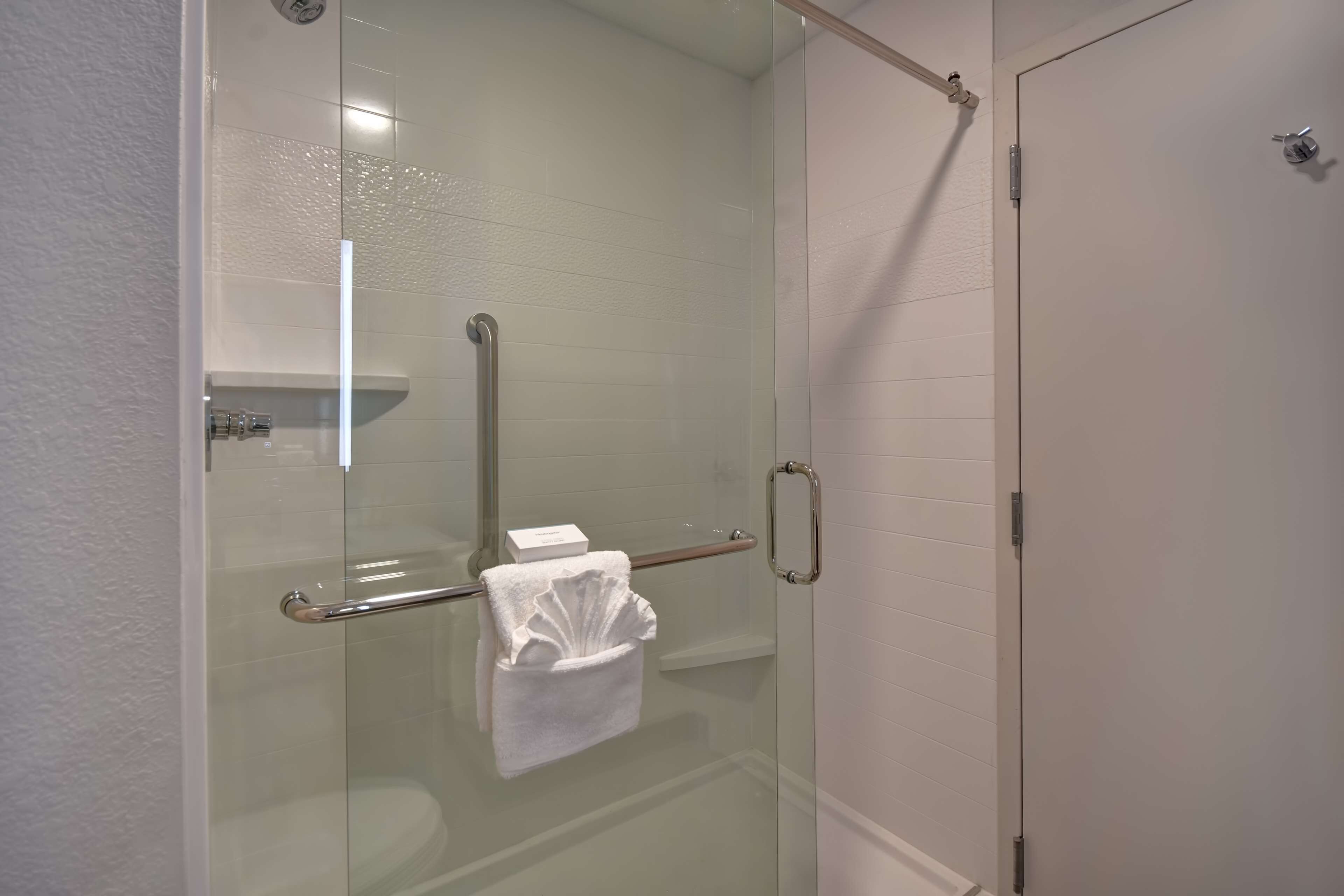 A glass-enclosed shower with a glass door, a towel rack, and a small shelf with toiletries.