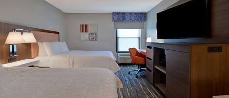 A hotel room with two beds, a desk, a television, and a window with a view.