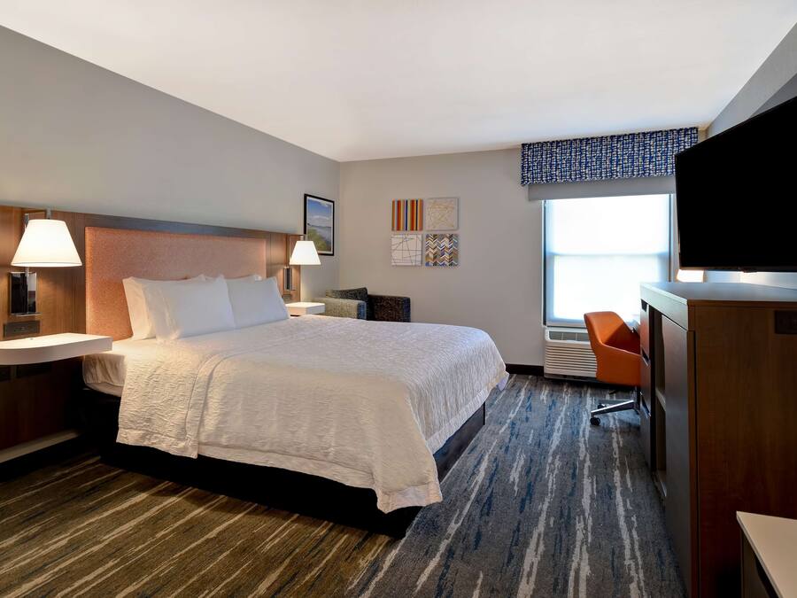 A hotel room with a large bed, bedside lamps, a flat-screen TV, a desk, and a chair.