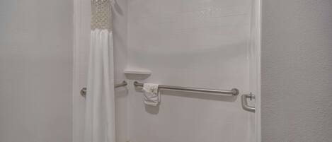 A shower area with a white tiled wall, a shower curtain, a grab bar, and a towel rack.