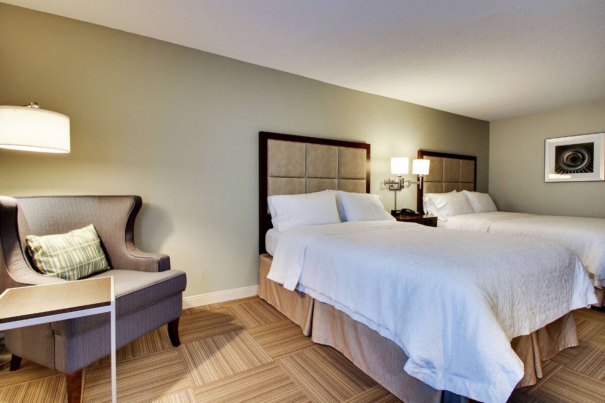 Habitació d'hotel amb dos llits, una cadira, un escriptori i una làmpada.
