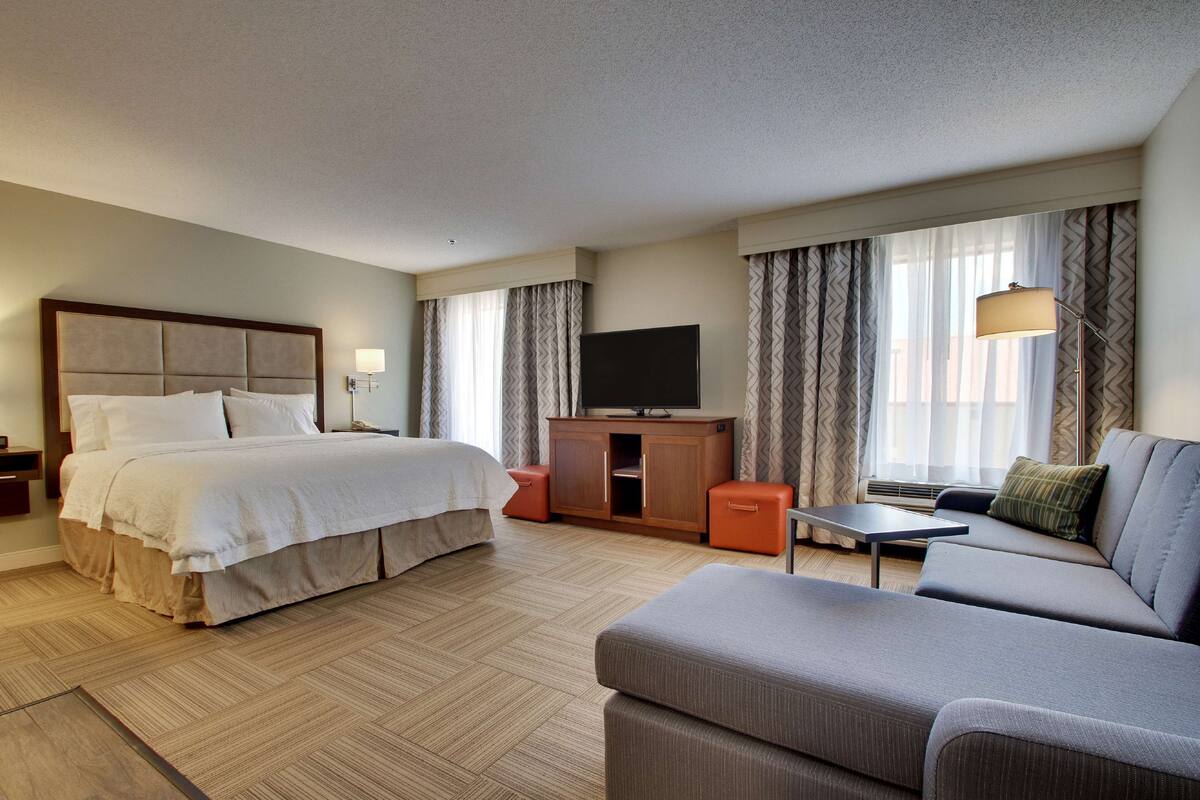 A hotel room with a large bed, a sofa, a TV, and a desk.