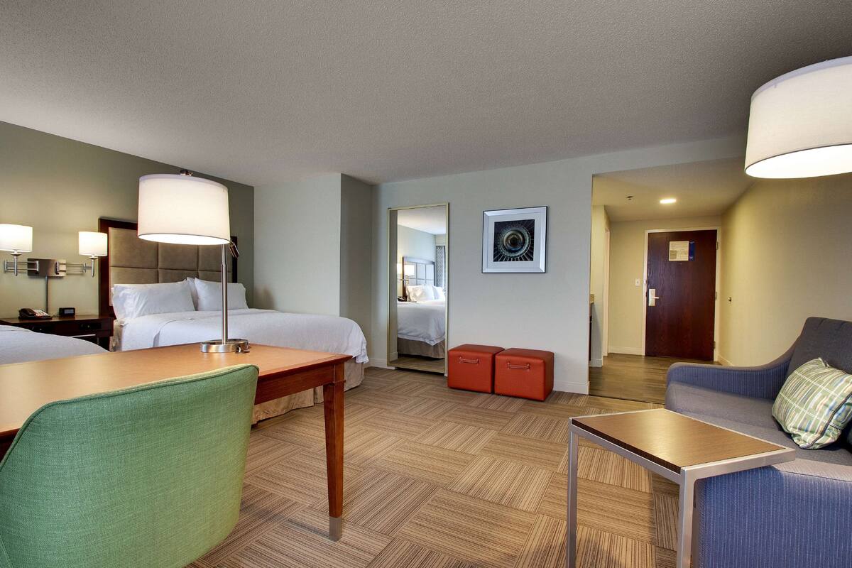 A hotel room with a bed, a desk, a chair, a sofa, and a small table.