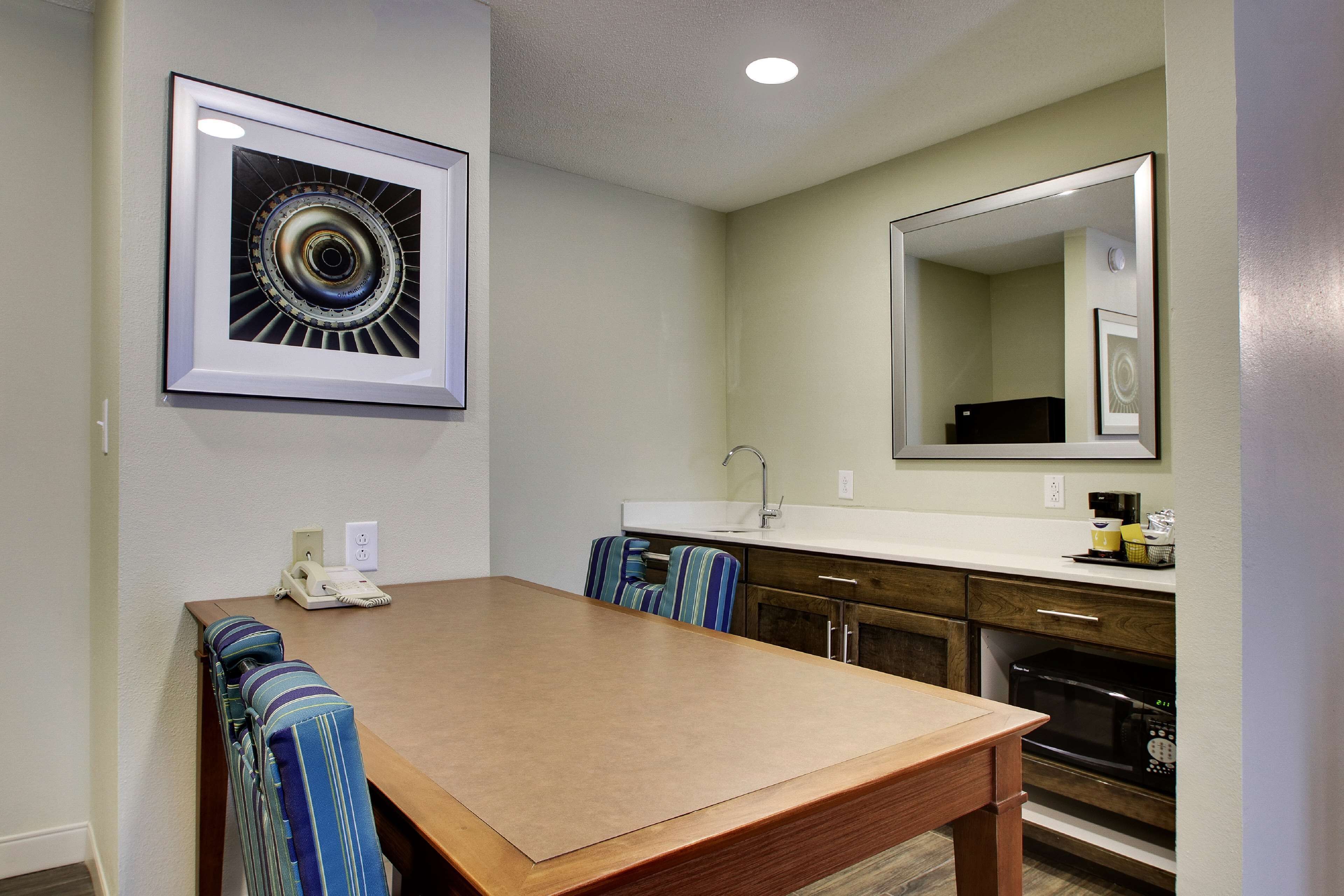 A dining area with a wooden table and chairs, a kitchen with a microwave and sink, and framed artwork on the walls.
