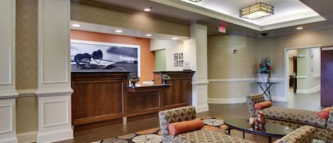 A lobby with a reception desk, patterned sofas, a coffee table, and a decorative plant.