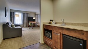 A compact hotel room with a kitchenette, a sofa, a dining area, and a television. - Hampton Inn Warner Robins (Warner Robins)