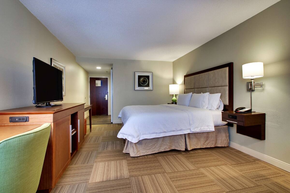 A hotel room with a bed, desk, television, and a lamp.