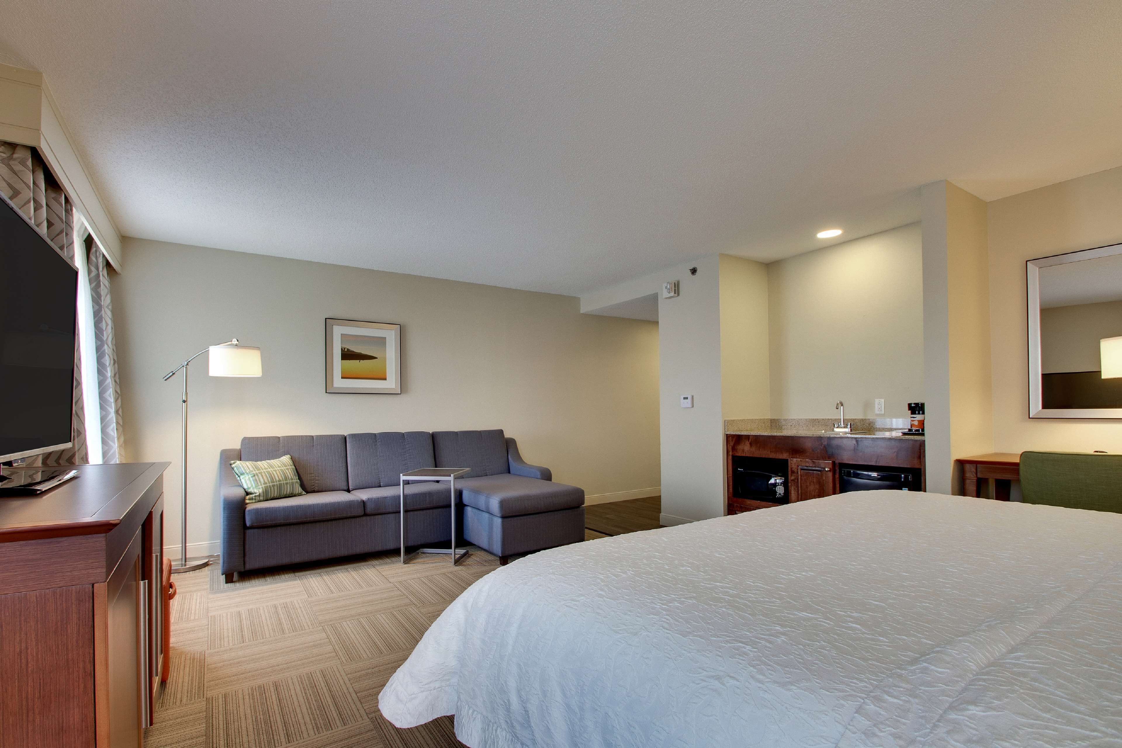Habitación de hotel con una cama grande, un sofá, un escritorio, un televisor de pantalla plana, una cafetera y una pequeña kitchenette.