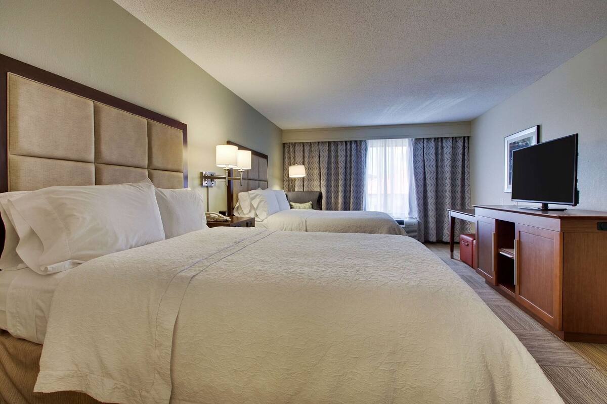 A hotel room with two beds, a TV, a desk, and a chair.