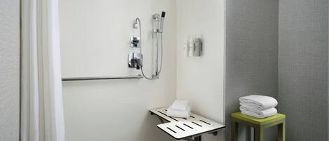 A bathroom with a shower, grab bar, and a small table with towels.