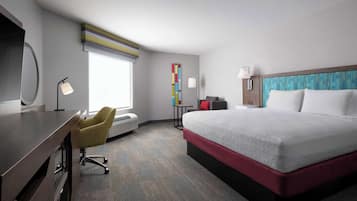 Habitación de hotel con una cama grande, un escritorio con una silla, una mesita y una ventana con persianas.