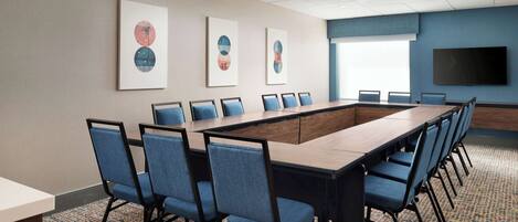 A conference room with a long table, blue chairs, and framed artwork on the wall.