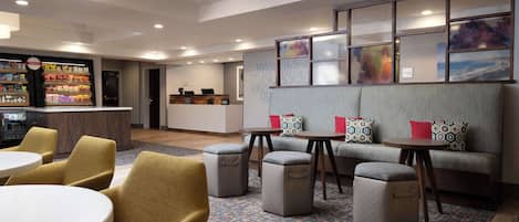 A modern hotel lobby with seating areas, a reception desk, and a snack bar.