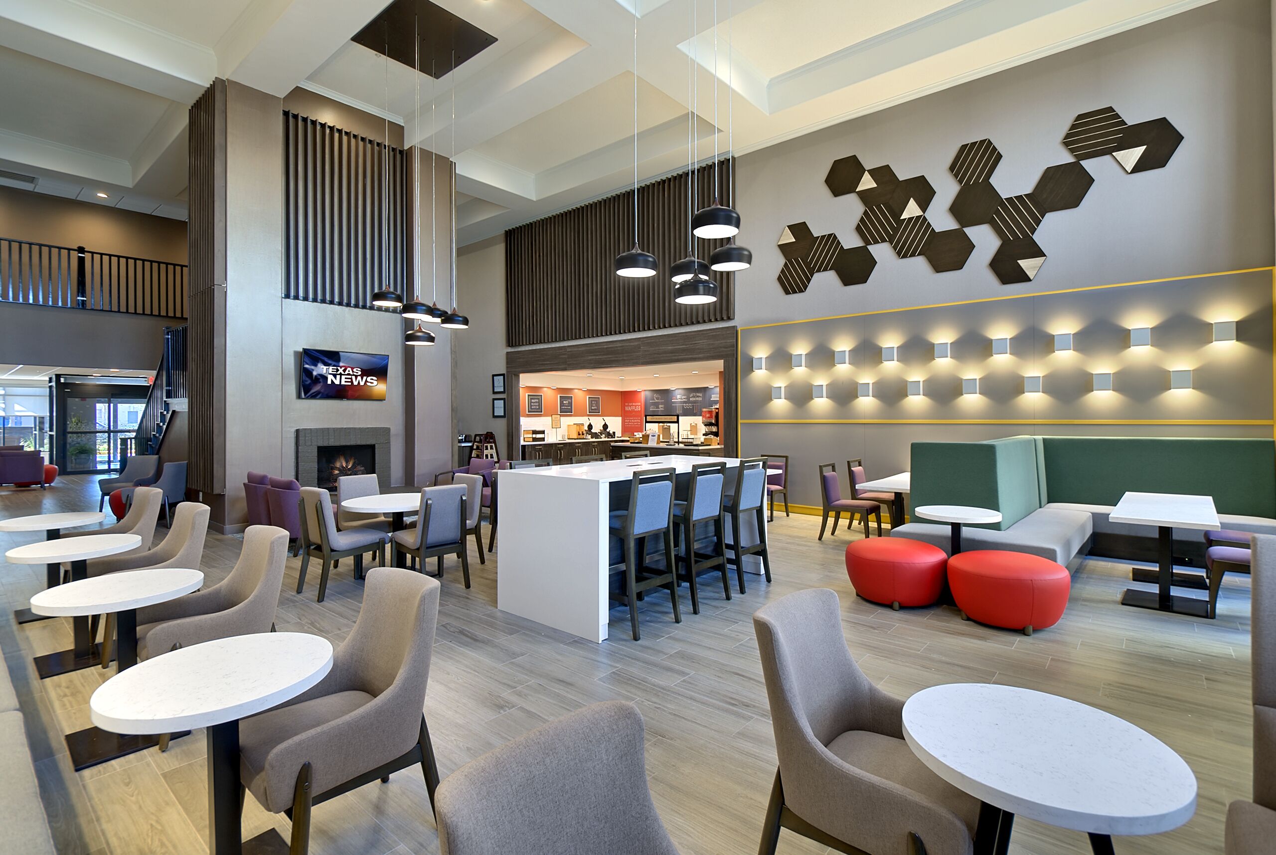 A modern lounge area with multiple seating options, including round tables and chairs, a central island with bar stools, and a decorative wall with geometric patterns.