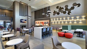 A modern lounge area with multiple seating options, including round tables and chairs, a central island with bar stools, and a decorative wall with geometric patterns.