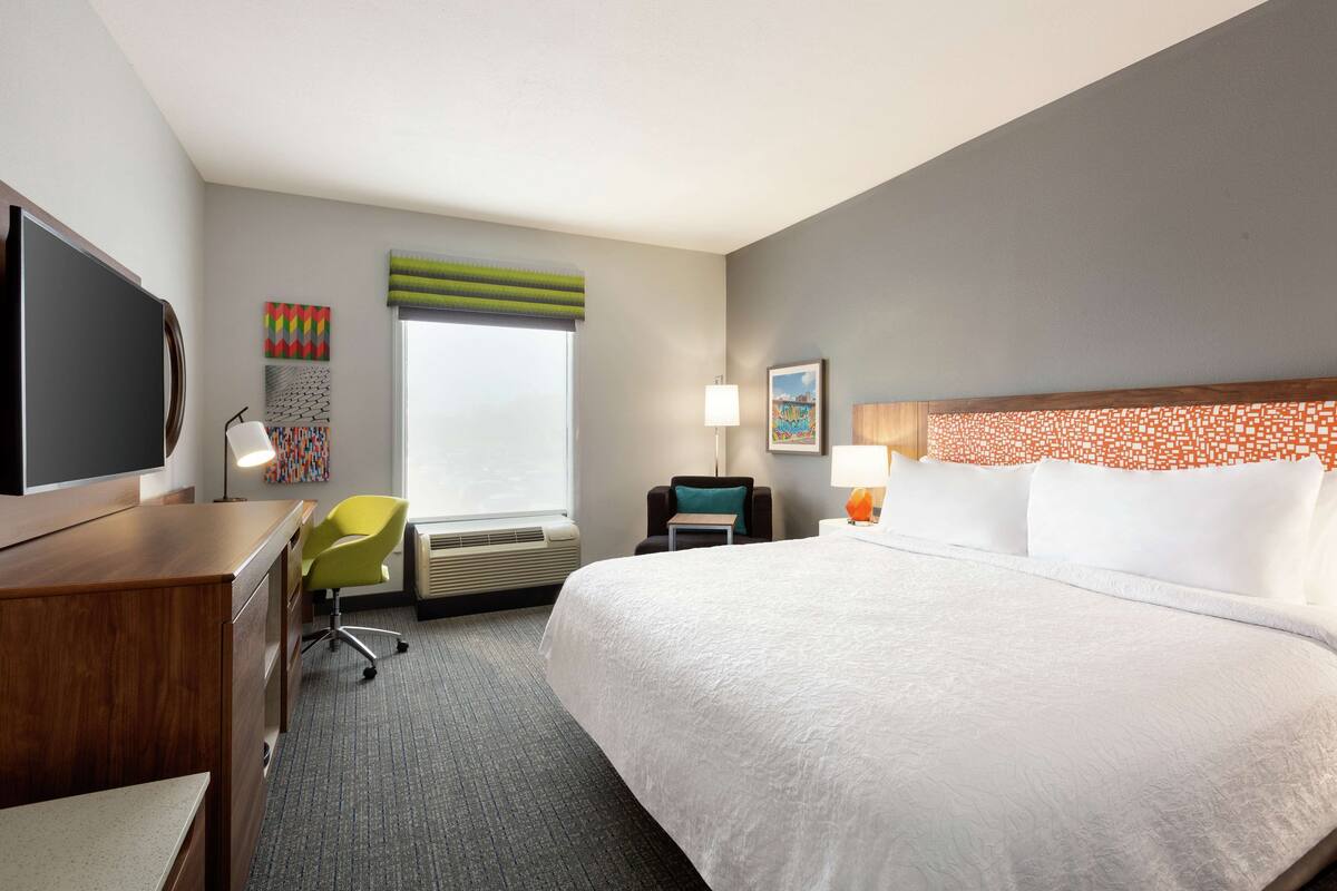 A hotel room with a large bed, a desk, a chair, a TV, and artwork on the walls.
