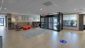 A modern lobby with a beige sofa, red ottomans, a glass door entrance, and framed artwork on the walls. - Hampton Inn & Suites Houston-Cypress Station (Houston)