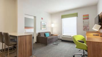 A modern hotel room with a sofa, a desk, a chair, and a small table.