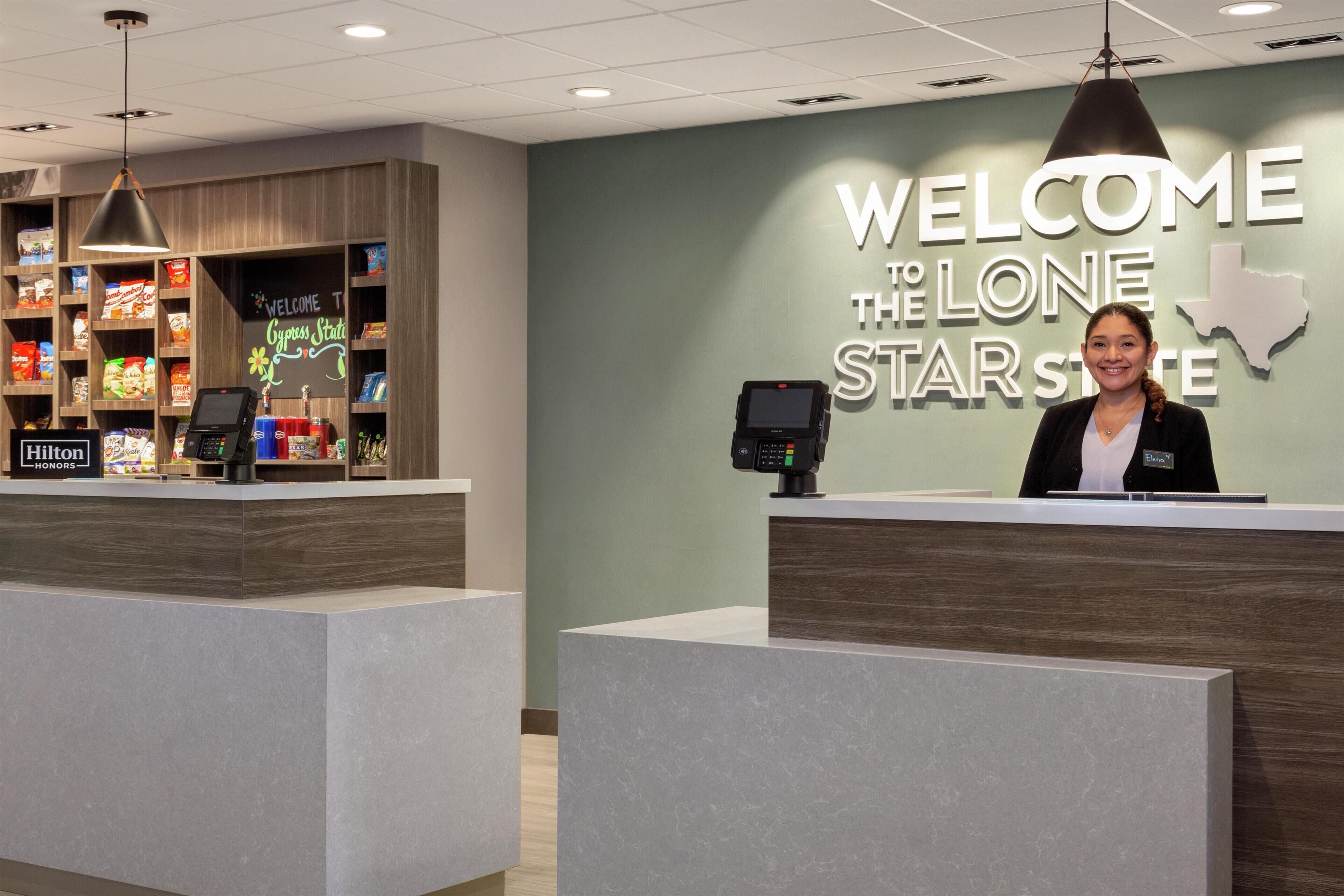 A hotel reception area with a 'Welcome to the Lone Star State' sign, a digital kiosk, and a display of local snacks.