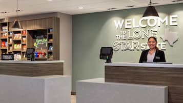 A hotel reception area with a 'Welcome to the Lone Star State' sign, a digital kiosk, and a display of local snacks.