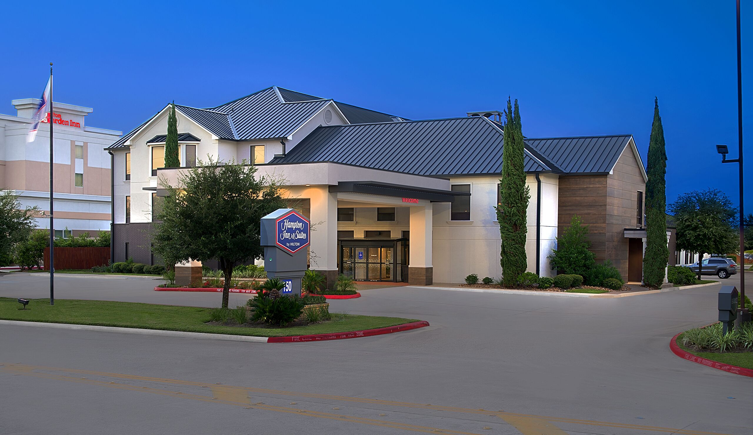 A Hampton Inn by Hilton hotel with a modern design, a welcoming entrance, and a landscaped driveway.