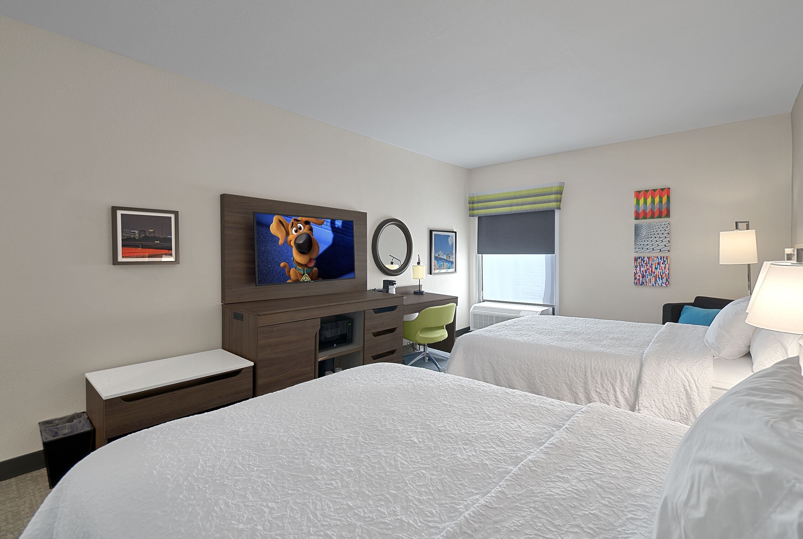 Ein Hotelzimmer mit zwei Betten, einem Fernseher, einem Schreibtisch und einem Sessel.