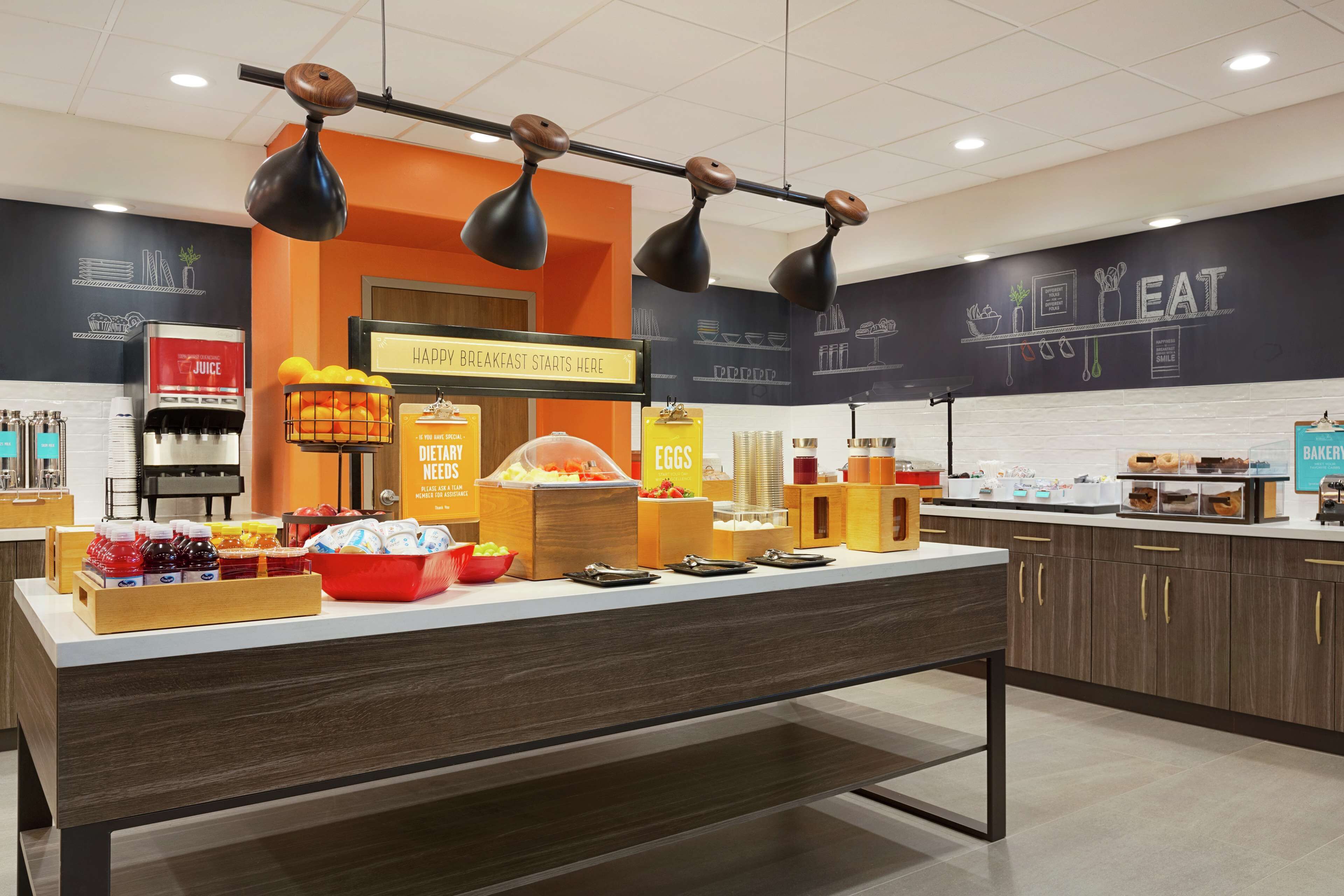 A breakfast bar with various food items and a juice dispenser.