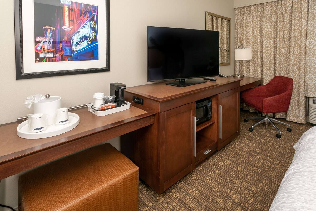 Een hotelkamer met een houten bureau, een televisie, een rode stoel, een magnetron en een koffiehoek.