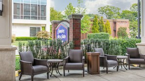 Ein Patio mit Korbmöbeln, ein Schild für Hampton Inn & Suites und ein modernes Gebäude im Hintergrund.