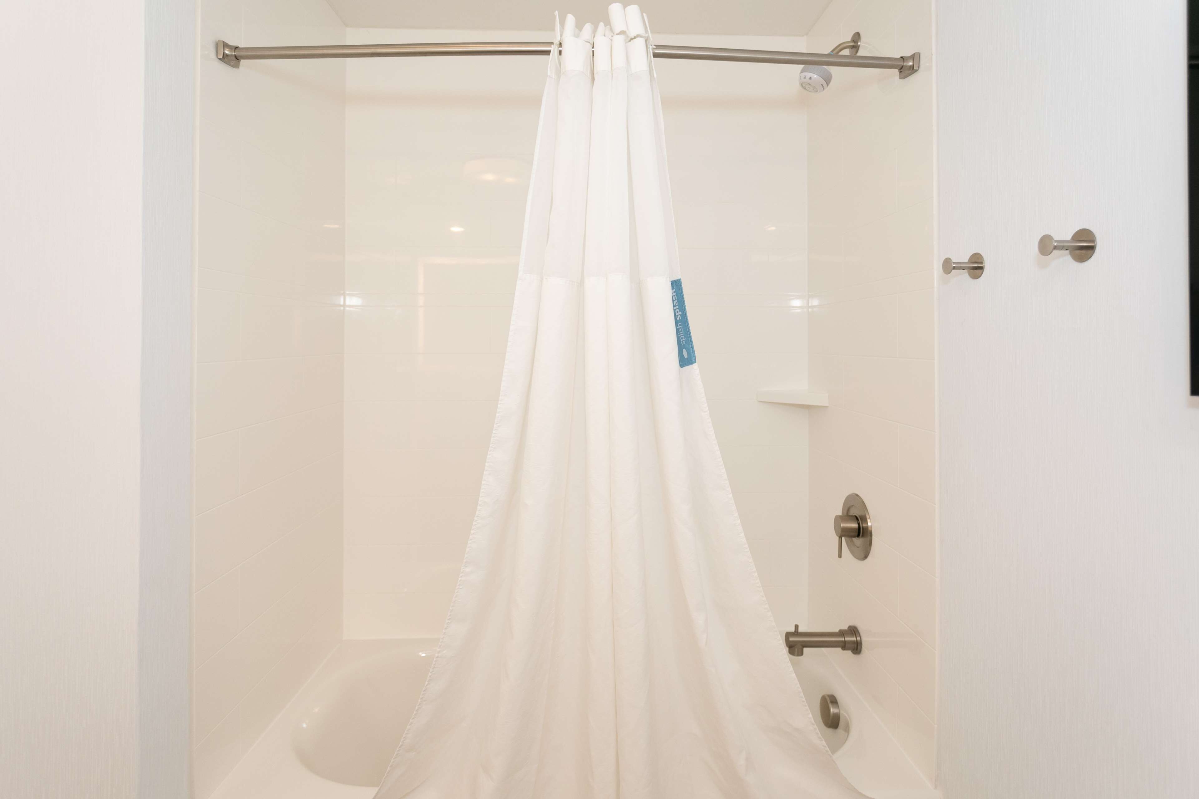A shower with a white curtain and a glass door.