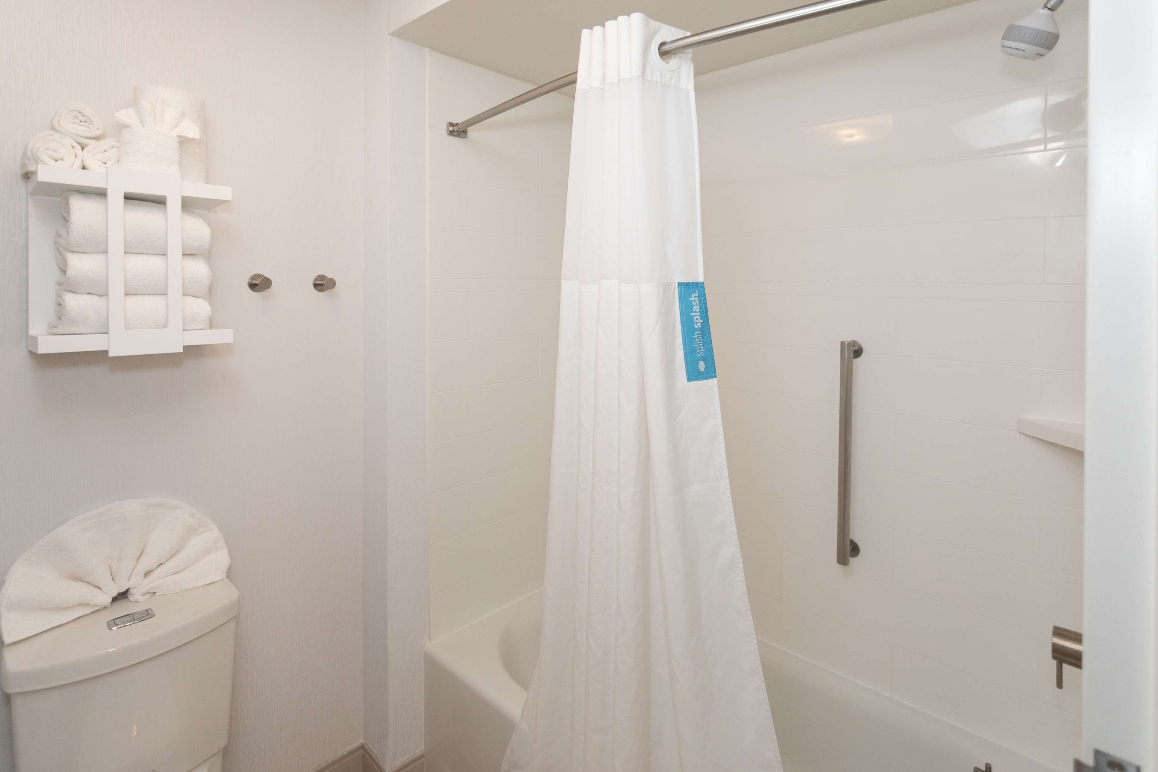 Un baño con inodoro blanco, cortina de ducha y un perchero con toallas dobladas.