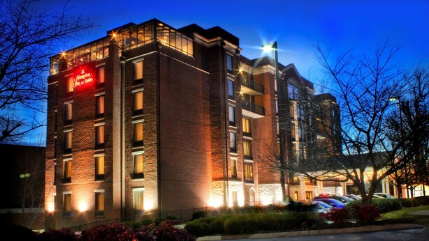 Ein mehrstöckiges Hotel mit Backsteinfassade, beleuchteten Fenstern und einem sichtbaren Schild, das es als Hampton Inn & Suites kennzeichnet.