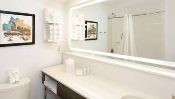 Un bagno con uno specchio grande, un water, un lavandino e una doccia. Asciugamani e articoli da toilette sono presenti sul ripiano.