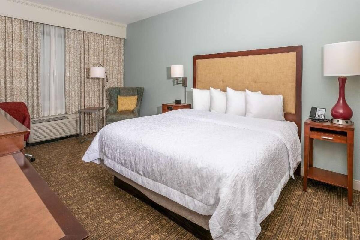 Een hotelkamer met een groot bed, twee nachtkastjes, een stoel, een bureau en een lamp.