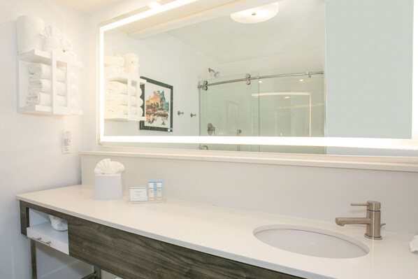 Un baño con un espejo grande, un lavabo, un perchero para toallas y una ducha.